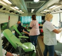 krwiodawcy siedzą na fotelach w ambulansie, którego obsługa prowadzi pobór krwi.