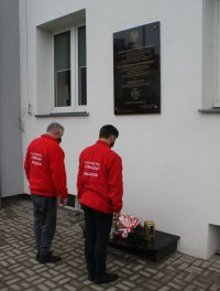 dwóch mężczyzn przed tablicą pamiątkową przed budynkiem - stoją tyłem.