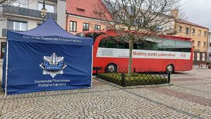 Mobilny punkt poboru krwi i namiot z napisem Komenda Powiatowa Policji w Łęczycy na rynku starego miasta w Łęczycy.