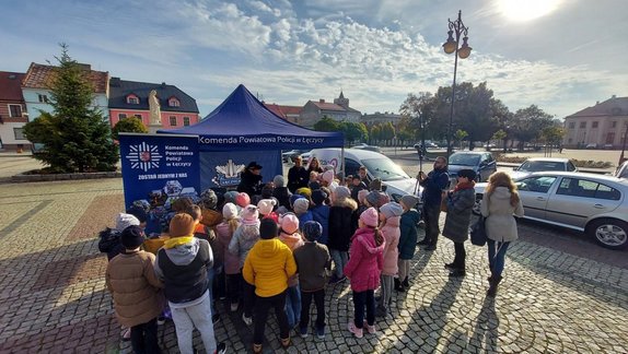 Dzieci stoją tyłem przed namiotem promocyjny Komendy Powiatowej Policji w Łęczycy