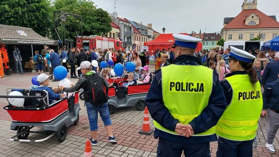 Policjanci stoją tyłem w tle uczestnicy pikniku mundurowego na placu Tadeusza Kościuszki