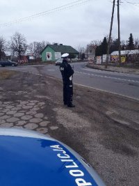 policjant obok radiowozu na drodze.