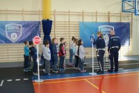 Policjanci z dziećmi podczas wydarzenia na sali z rozłożonym torem w zakresie wiedzy ruchu drogowego.