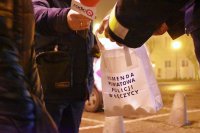 Policjant trzyma białą torbę z napisem Komenda Powiatowa Policji w Łęczycy. W ręku mężczyzny mikrofon z logiem  RadioQ .