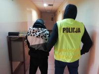 policjant w kamizelce z napisem POLICJA obok zatrzymany. Obaj stoją tyłem.