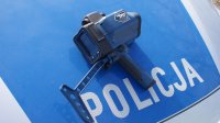 laserowy miernik prędkości położony na masce samochodu. Tło koloru niebieskiego napis POLICJA.