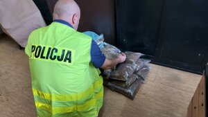 policjant w kamizelce z napisem POLICJA z zabezpieczonym tytoniem w workach foliowych.