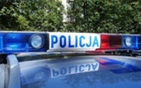 Dach policyjnego radiowozy z sygnałami i napisem POLICJA. W tle drzewa.