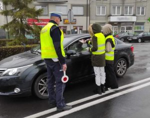 Policjant obok samochodu z dziećmi wręczają ulotki.