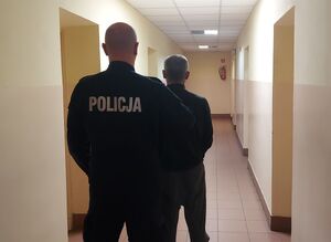 policjant w mundurze z zatrzymanym stoją tyłem.