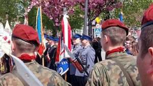 Policjanci z Pocztem Sztandarowym podczas uroczystości. W tle wojsko i uczestnicy obchodów.