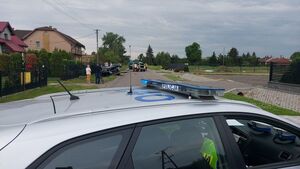 Prosty odcinek drogi, na którym stoją samochody biorące udział w zdarzeniu. Na pierwszym planie radiowóz z policjantami wewnątrz.