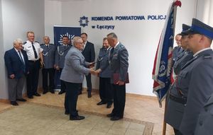 Komendant Powiatowy Policji w Łęczyc podczas  uroczystości w sali odpraw wraz z policjantami i zaproszonymi osobami.