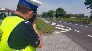 Policjant w kamizelce odblaskowej podczas pomiaru prędkości jadących pojazdów.