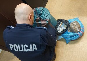 Policjant z zabezpieczonym tytoniem i papierosami w workach foliowych.