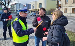 Policjanci wraz z przedstawicielami radia Q wręczają kwiaty i odblaski Paniom na terenie Łęczycy.