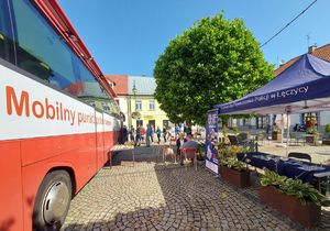 Mobilny punkt poboru krwi, obok stoisko promocyjne policji . W tle krwiodawcy przed ambulansem.