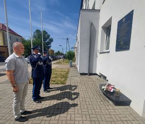 Dwóch policjantów i mężczyzna oddają honory przed grobem i tablicą.