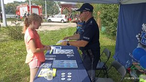 Policjant z dziećmi i uczestnikami wydarzenia nad zalewem miejskim w Łęczycy.