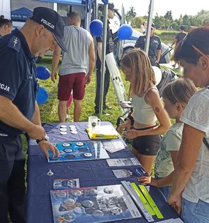 Policjant z dziećmi i uczestnikami wydarzenia nad zalewem miejskim w Łęczycy.