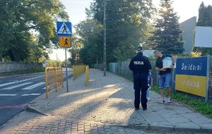 Policjantka z dziećmi na chodniku obok przejścia dla pieszych.