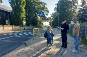 Policjantka z dziećmi na chodniku obok przejścia dla pieszych.
