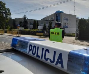 Policjant obok radiowozu mierzy prędkość.