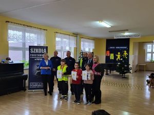 W szkole policjanci wraz z gronem pedagogicznym wręczają dzieciom nagrody.