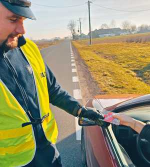 Umundurowany policjant wręczający zapachowe serduszko osobie kontrolowanej.