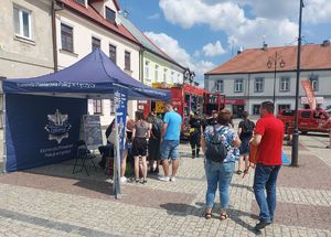 Stoisko policyjne z radiowozem na placu Kościuszki w Łęczycy podczas pikniku mundurowego oraz mieszkańcy miasta.