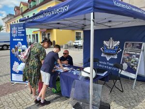 Stoisko policyjne z radiowozem na placu Kościuszki w Łęczycy podczas pikniku mundurowego oraz mieszkańcy miasta.