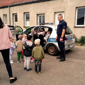 Przedszkolaki z policjantem obok radiowozu.