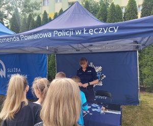 POLICJANTKA NA STOISKU PROMOCYJNYM Z ODWIEDZAJĄCYMI DZIEĆMI.