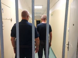 Policjant z zatrzymanym za kratą.