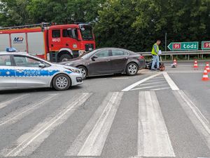 Policjant podczas oględzin miejsca zdarzenia. Radiowóz, samochód strażacki i osobówka.