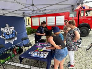 Stoisko promocyjne na pikniku z odwiedzającymi, policjantkami i gadżetami.