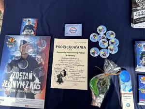 Stoisko promocyjne na pikniku z odwiedzającymi, policjantkami i gadżetami.