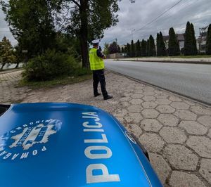 Policjant obok radiowozu prowadzi pomiar prędkości.