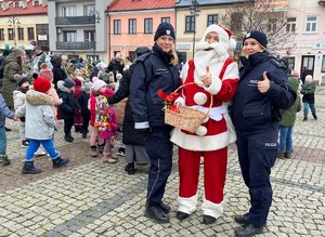 Policjantki wieszają na choince odblaski, w tle młodzież, mikołaj.