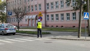 POLICJANT OBOK RADIOWOZU W REJONIE PRZEJŚCIA DLA PIESZYCH.