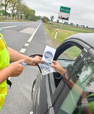 Policjantka trzyma ulotkę kampanii. W tle droga.