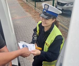 Policjantka trzyma ulotkę kampanii. W tle droga.