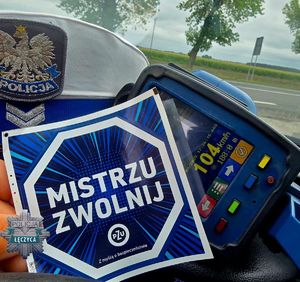 Policjantka trzyma ulotkę kampanii. W tle droga.