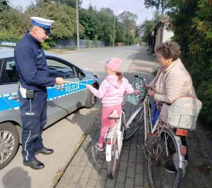 Policjant  i policjantka wręcza odblask. Czapka policyjna z odblaskiem.