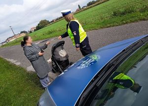 Policjant  i policjantka wręcza odblask. Czapka policyjna z odblaskiem.