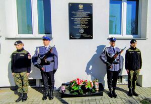 Delegacje składające kwiaty przed tablicą.