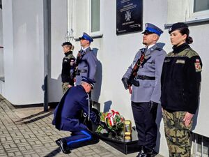 Delegacje składające kwiaty przed tablicą.