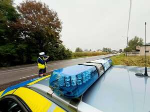 Policjant obok radiowozu mierzy prędkość.