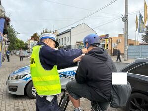 Policjant zakłada kask rowerzyście.