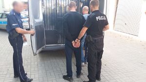 Dwóch policjantów z zatrzymanym przed radiowozem.